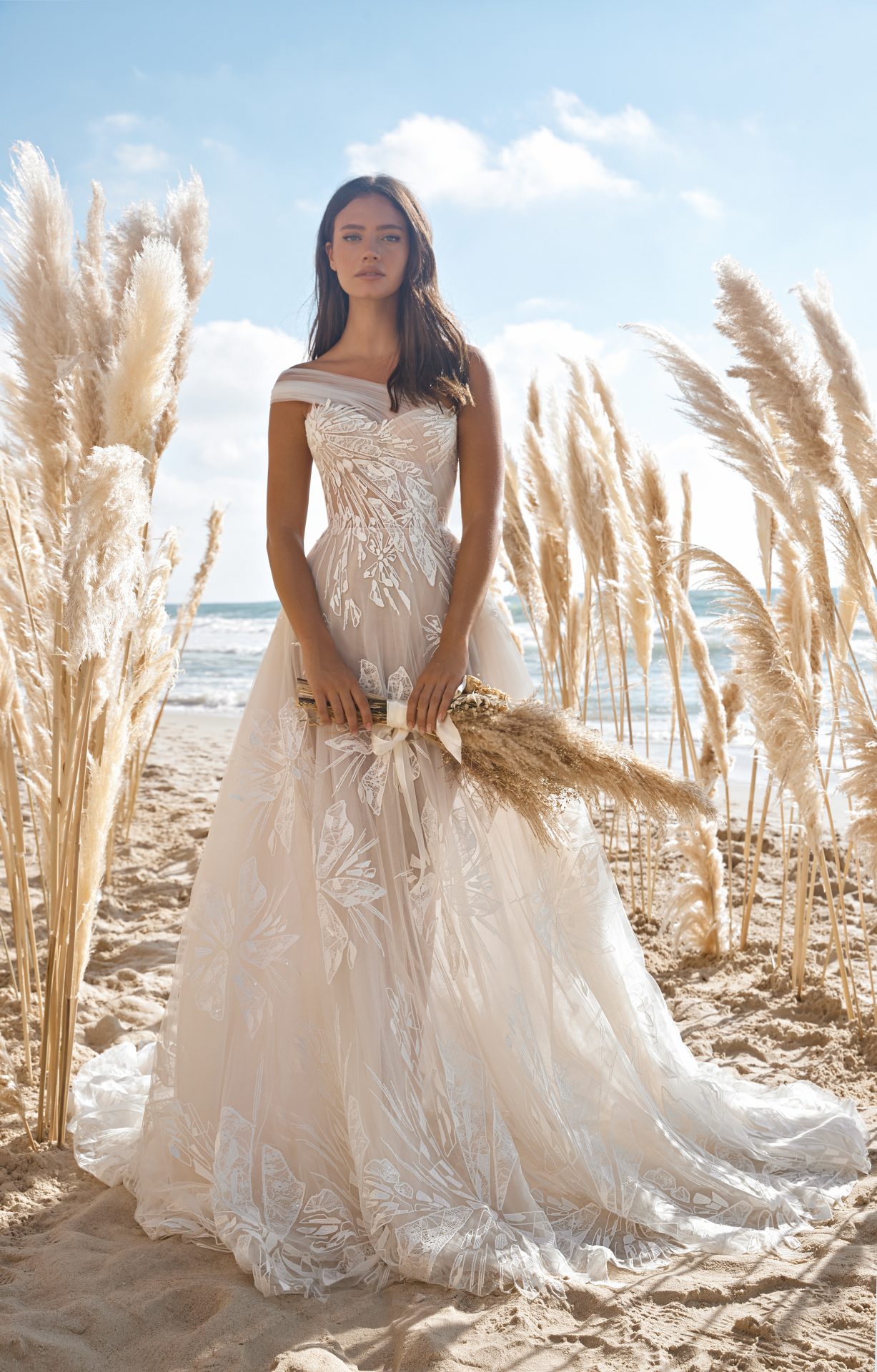 bride on a beach wearing lee petra grebenau raven wedding dress made of lace and tulle sold at dimitras bridal in chicago